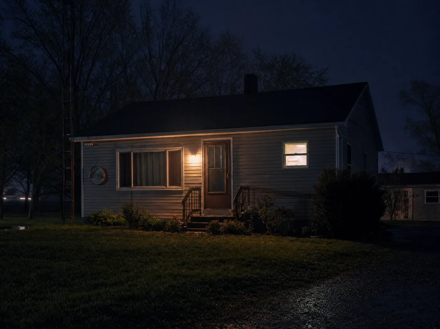 A house at night with the porch light on and one window lit